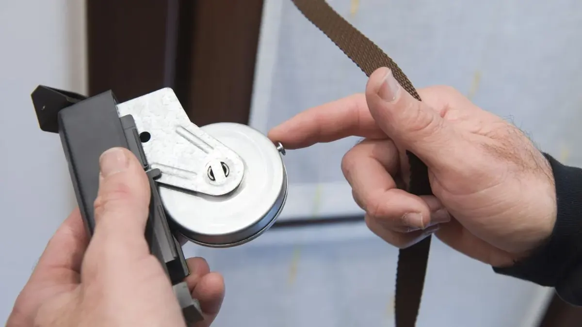 Manos reparando el mecanismo de eje y cinta de una cortina de enrollar