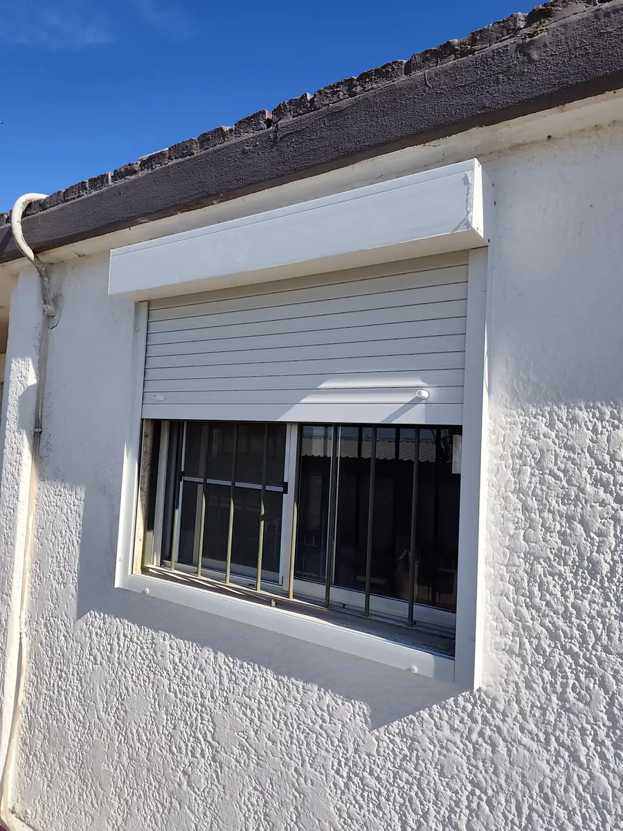 Cortina de enrollar blanca a media altura en fachada de estuco blanco, Ciudad de la Costa